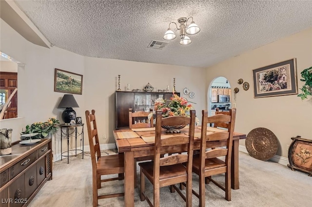 dining room with a chandelier, visible vents, arched walkways, and light colored carpet