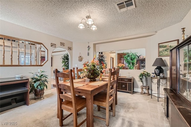 dining area featuring light carpet, visible vents, arched walkways, an inviting chandelier, and a textured ceiling