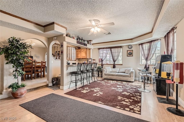 living room featuring arched walkways, light wood-style flooring, visible vents, and a wealth of natural light