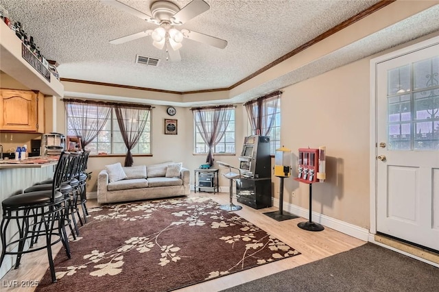 living area with crown molding, visible vents, light wood-style floors, ceiling fan, and a textured ceiling