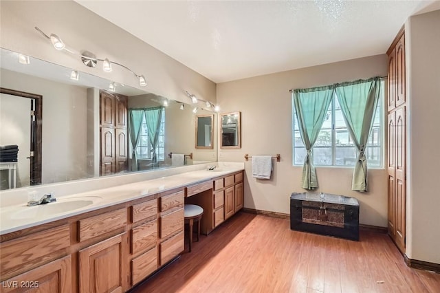 full bath featuring double vanity, baseboards, a sink, and wood finished floors