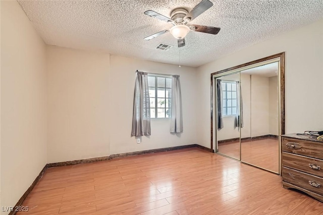 unfurnished bedroom featuring light wood finished floors, visible vents, a ceiling fan, a textured ceiling, and a closet