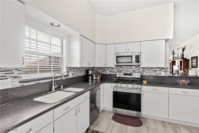 kitchen with appliances with stainless steel finishes, dark countertops, a sink, and white cabinets