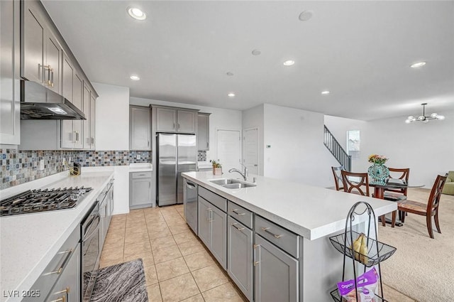 kitchen featuring decorative backsplash, appliances with stainless steel finishes, gray cabinets, a sink, and exhaust hood