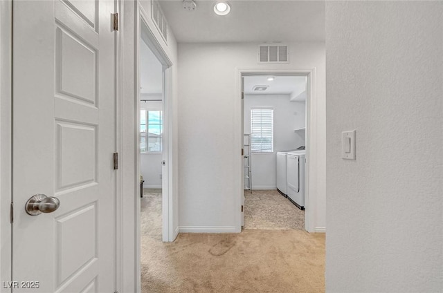 corridor featuring light carpet, baseboards, visible vents, and washing machine and clothes dryer