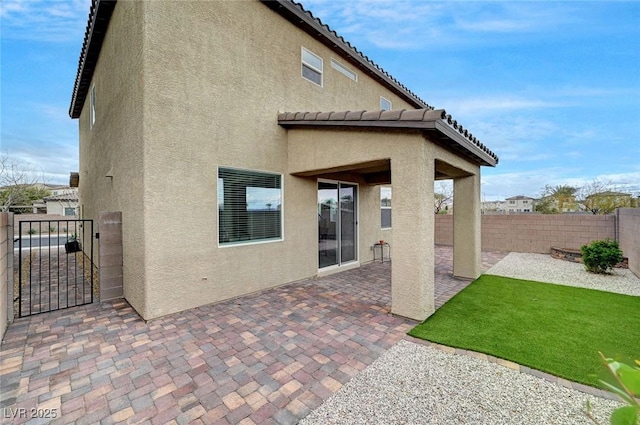 rear view of house featuring stucco siding, a gate, a patio area, fence, and a tiled roof