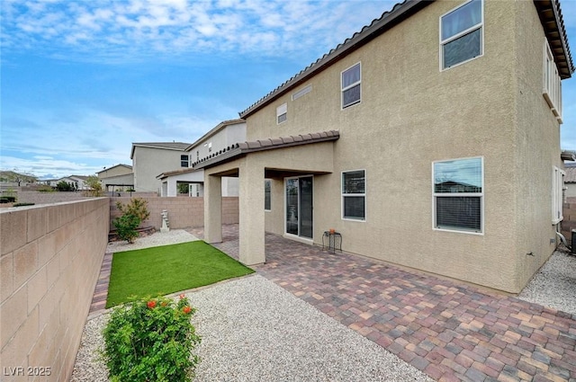 rear view of house featuring a fenced backyard, a tiled roof, a patio, and stucco siding