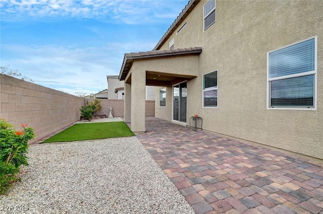 exterior space with a fenced backyard, a tile roof, a patio, and stucco siding