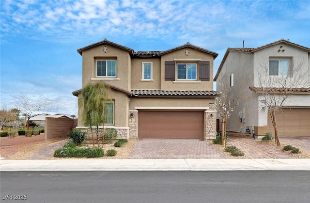 mediterranean / spanish-style house with an attached garage, a tile roof, stone siding, decorative driveway, and stucco siding