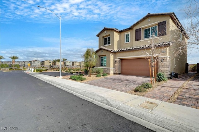 mediterranean / spanish house featuring a residential view, a tiled roof, an attached garage, decorative driveway, and stucco siding