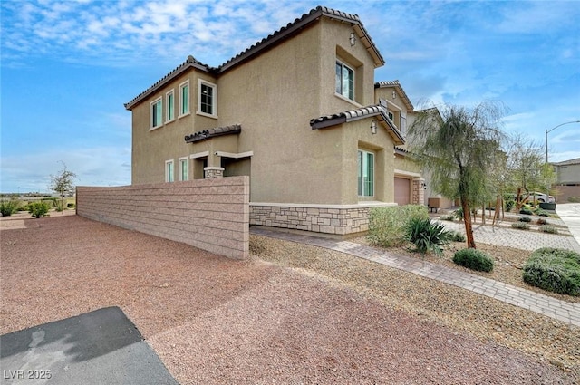 view of home's exterior featuring a garage, a fenced front yard, a tile roof, and stucco siding