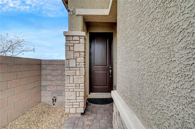 view of exterior entry featuring fence and stucco siding