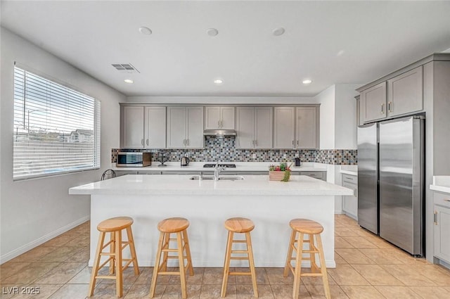 kitchen featuring visible vents, freestanding refrigerator, a sink, gray cabinetry, and backsplash