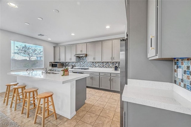 kitchen with stainless steel appliances, visible vents, gray cabinets, tasteful backsplash, and a kitchen bar