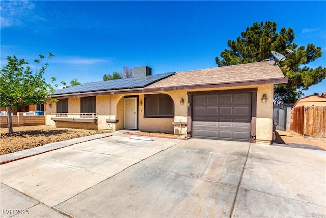 single story home featuring roof mounted solar panels, fence, stucco siding, driveway, and a garage