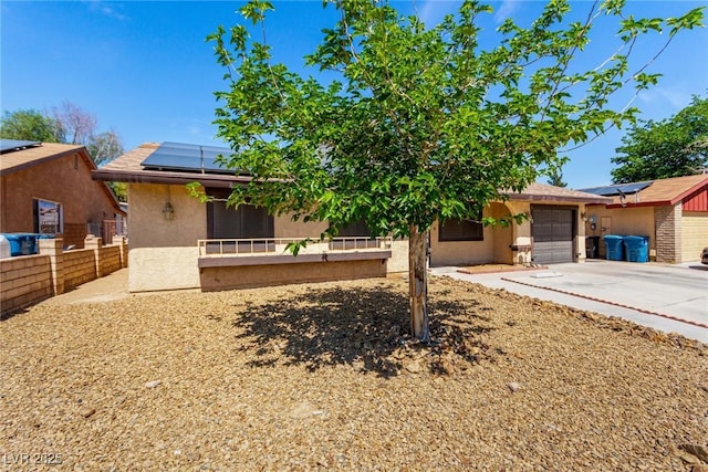 view of front of home with fence, stucco siding, solar panels, driveway, and a garage
