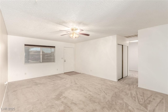 spare room with a textured ceiling, visible vents, light carpet, and ceiling fan