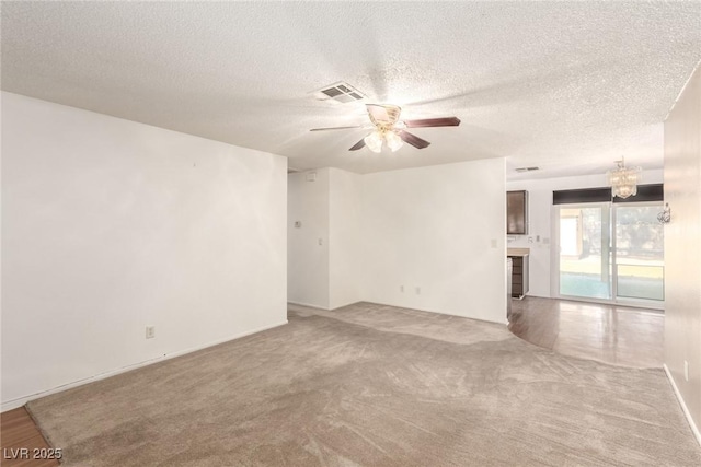unfurnished living room featuring ceiling fan with notable chandelier, carpet, visible vents, and a textured ceiling