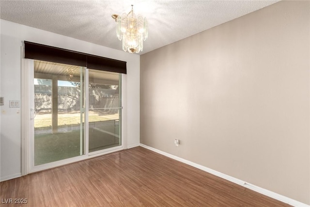 empty room featuring baseboards, wood finished floors, a textured ceiling, and a chandelier