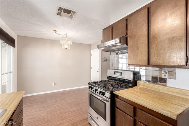 kitchen with under cabinet range hood, stainless steel gas range, baseboards, a notable chandelier, and visible vents