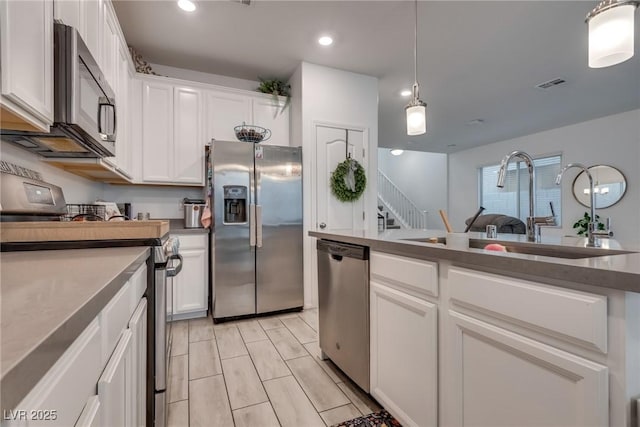 kitchen featuring visible vents, stainless steel appliances, white cabinetry, pendant lighting, and a sink