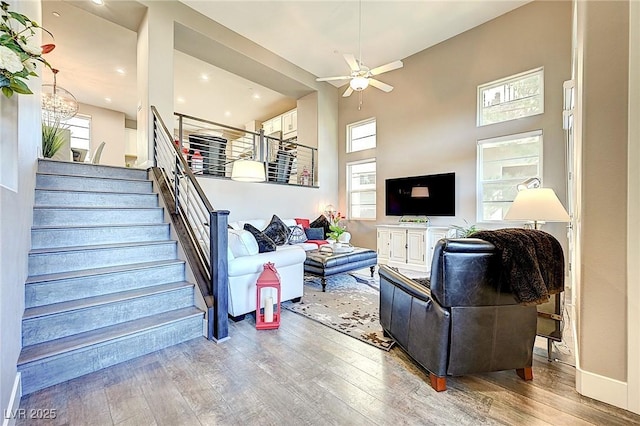 living area featuring a towering ceiling, baseboards, stairs, a ceiling fan, and wood-type flooring