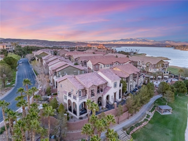 aerial view at dusk with a water view and a residential view