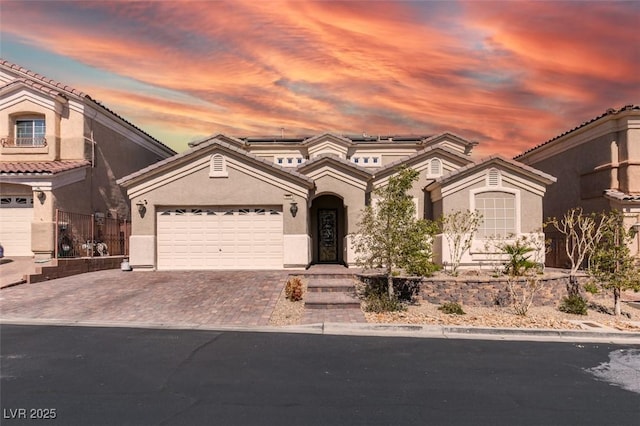 mediterranean / spanish-style house with fence, roof mounted solar panels, stucco siding, decorative driveway, and a garage