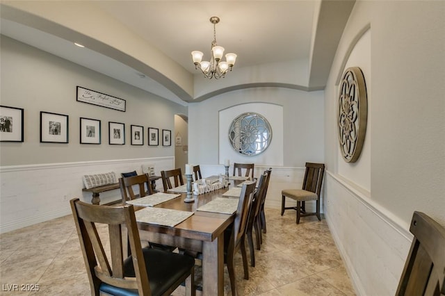 dining space with light tile patterned floors, arched walkways, a wainscoted wall, and a chandelier