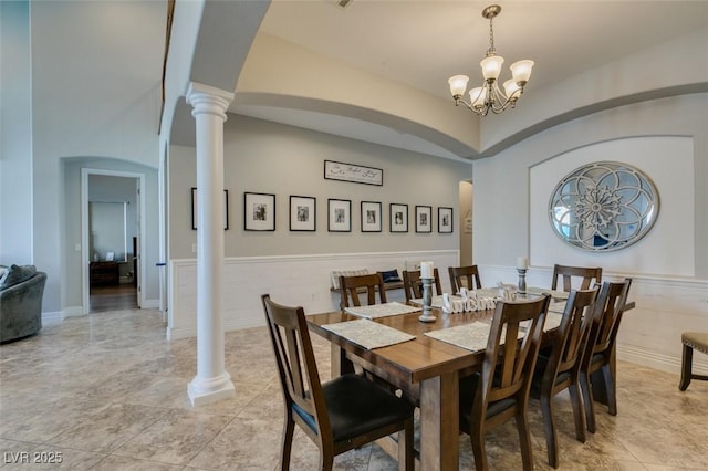 dining room featuring decorative columns, arched walkways, a chandelier, and wainscoting