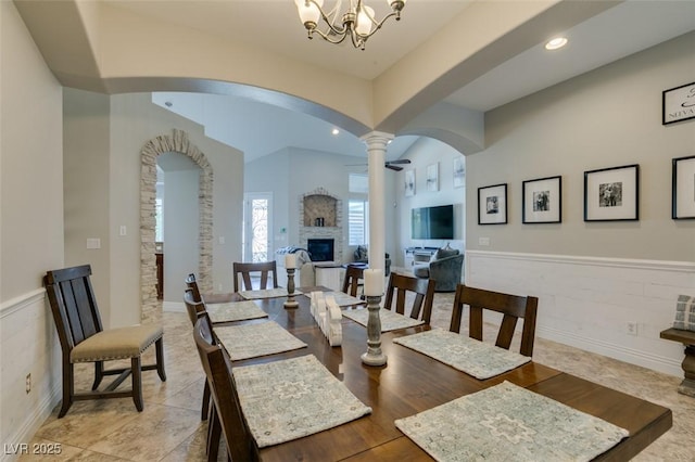 dining space featuring a notable chandelier, a glass covered fireplace, recessed lighting, arched walkways, and wainscoting