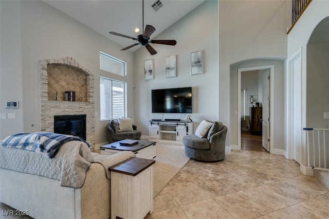 living area with visible vents, ceiling fan, a stone fireplace, arched walkways, and high vaulted ceiling