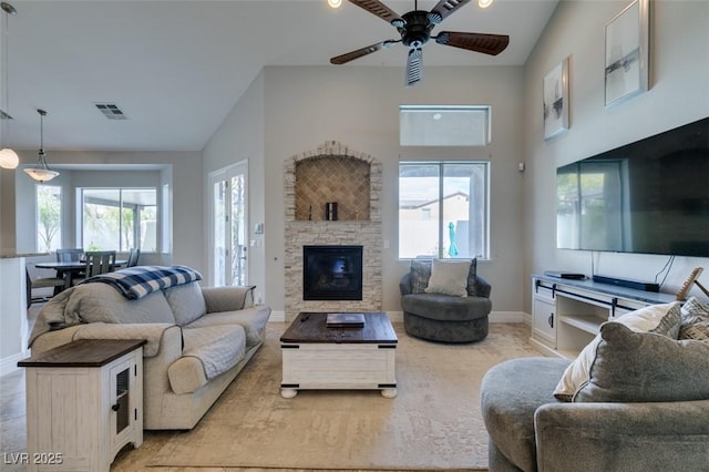 living room featuring visible vents, baseboards, ceiling fan, a stone fireplace, and high vaulted ceiling