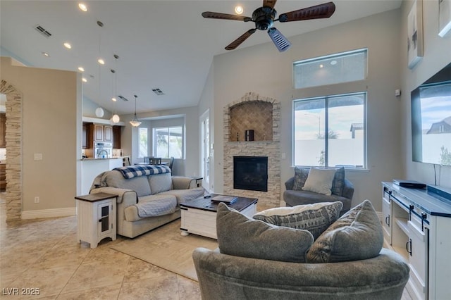 living area featuring a stone fireplace, light tile patterned flooring, visible vents, and high vaulted ceiling