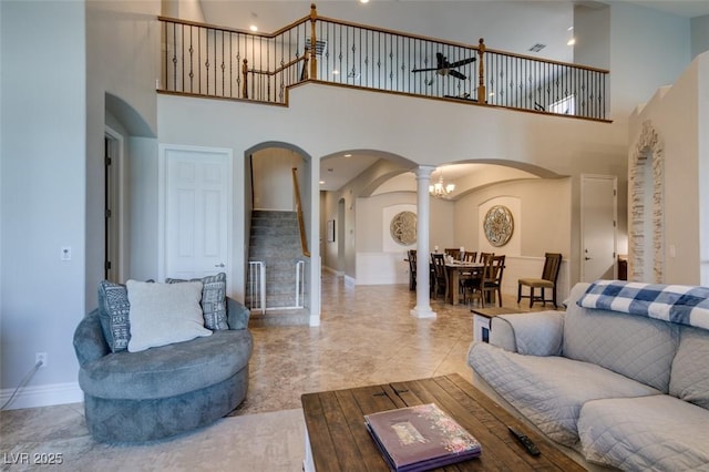 living room featuring baseboards, stairway, a high ceiling, arched walkways, and ornate columns