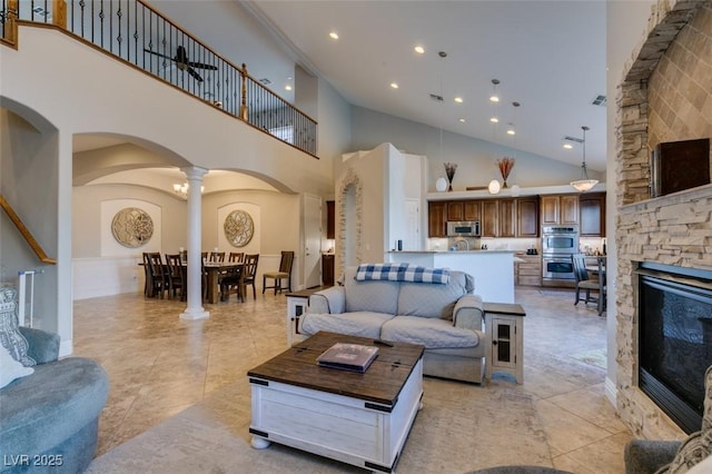 living area with a high ceiling, decorative columns, recessed lighting, arched walkways, and a stone fireplace