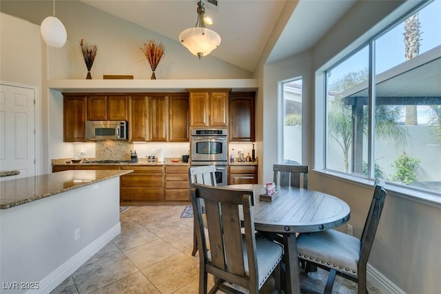 kitchen with hanging light fixtures, light stone counters, a wealth of natural light, and stainless steel appliances