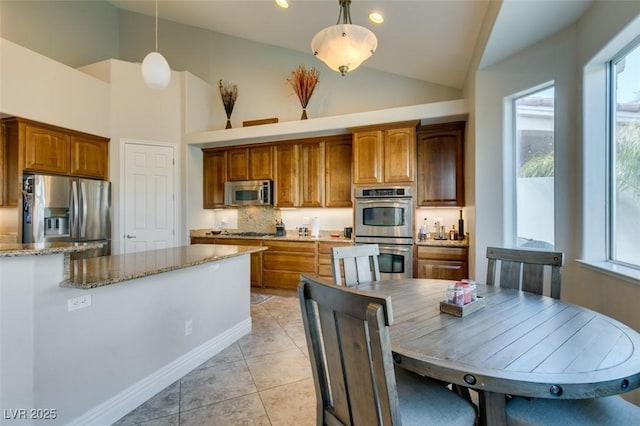 kitchen with decorative light fixtures, brown cabinets, appliances with stainless steel finishes, and light stone countertops