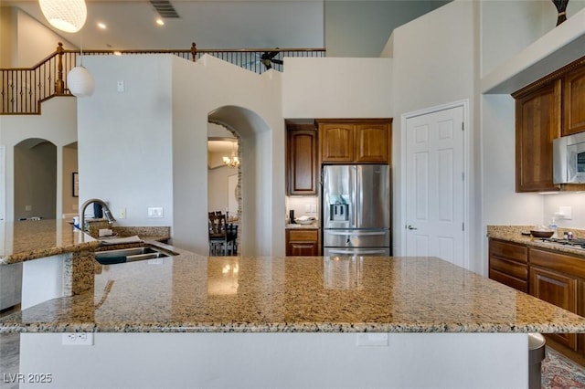 kitchen with visible vents, appliances with stainless steel finishes, a towering ceiling, arched walkways, and a sink