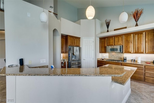 kitchen featuring brown cabinets, light stone counters, a high ceiling, appliances with stainless steel finishes, and a peninsula