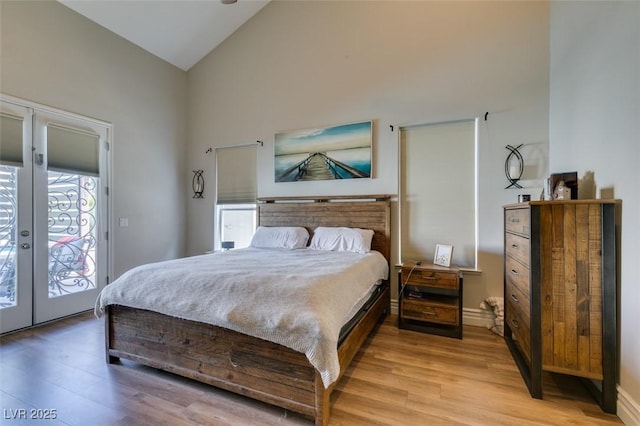 bedroom featuring high vaulted ceiling, access to outside, french doors, light wood finished floors, and baseboards