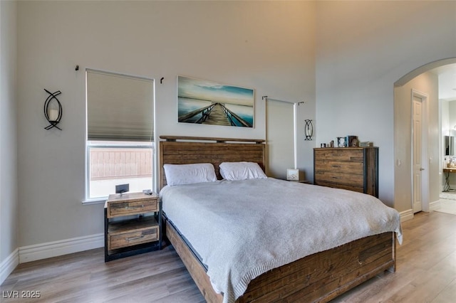 bedroom featuring wood finished floors, arched walkways, a towering ceiling, and baseboards