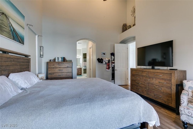 bedroom featuring ensuite bath, a high ceiling, wood finished floors, and arched walkways