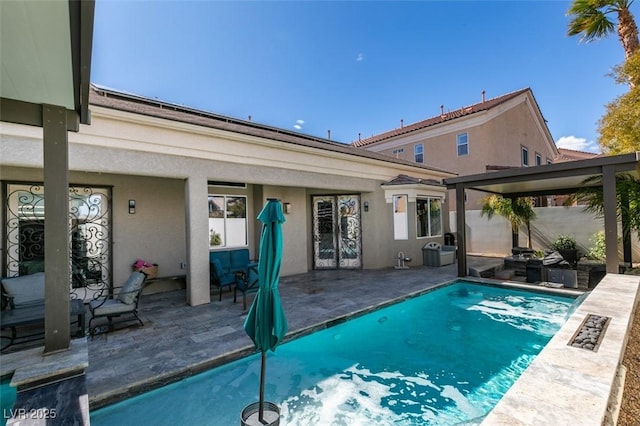 rear view of house with an outdoor pool, french doors, a patio, and stucco siding