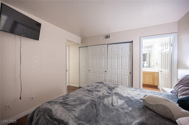 bedroom featuring visible vents, a textured ceiling, ensuite bath, wood finished floors, and baseboards