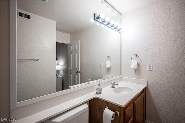 half bath featuring visible vents, a textured wall, and vanity