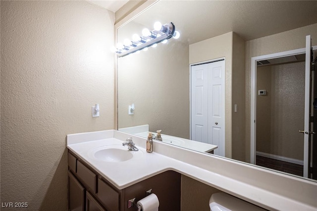 half bathroom featuring a textured wall, vanity, and toilet