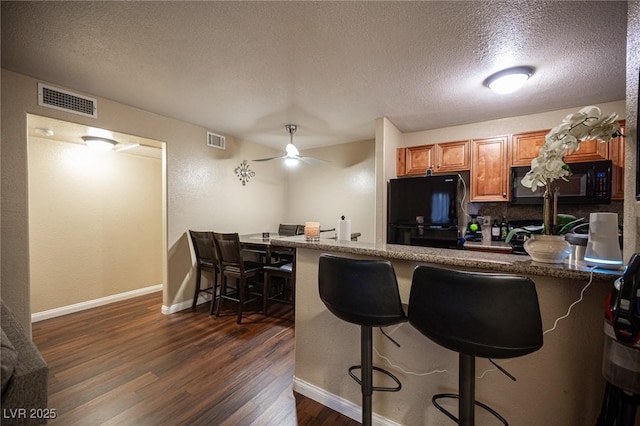 kitchen featuring black appliances, a kitchen bar, visible vents, and dark wood-type flooring