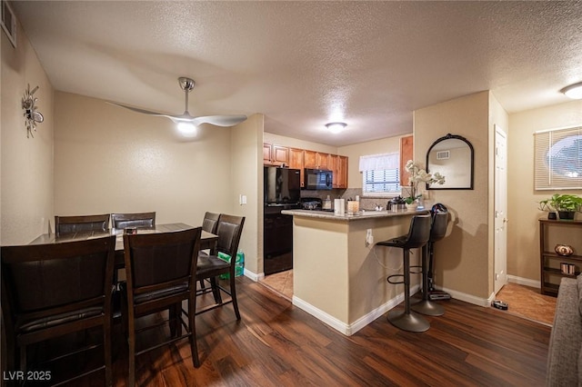 kitchen featuring dark wood-style flooring, ceiling fan, a peninsula, and black appliances