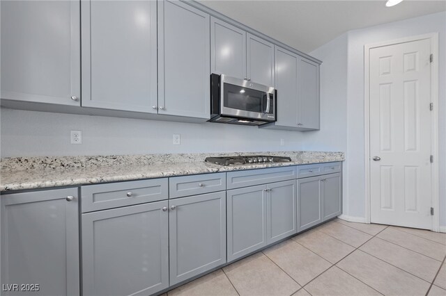 kitchen with light tile patterned flooring, gray cabinetry, stainless steel appliances, and light stone countertops